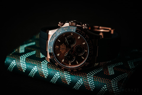 A rose gold Rolex Daytona with a chocolate dial resting on a green chevron leather case