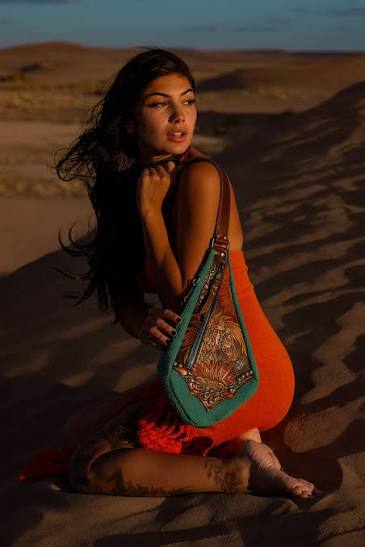 A woman carrying an orange and turquoise embroidered handbag in the desert